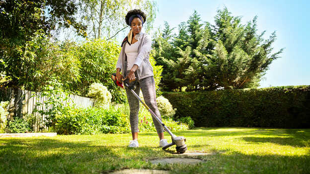 Femme utilisant le coupe-bordure sans fil Honda sur la pelouse d’un jardin.