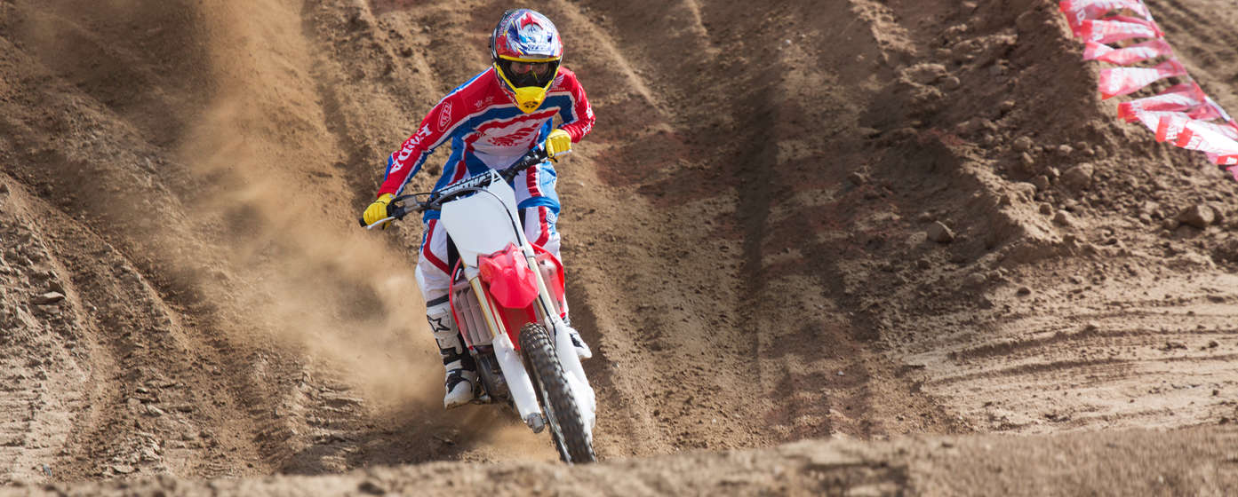 Front-facing CRF125R motorcycle with rider, on dirt track location.