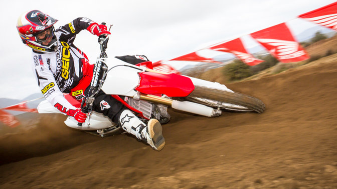 Vue de trois-quarts avant de la CRF250R inclin&eacute;e en courbe avec pilote. Sur chemin de terre.