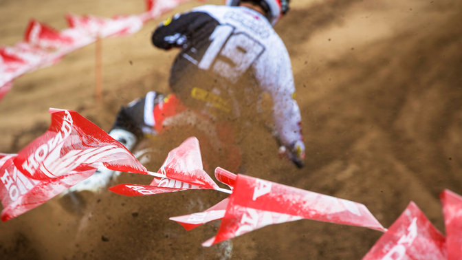 Vue arri&egrave;re du pilote sur une moto tout-terrain. L&eacute;g&egrave;rement inclin&eacute; vers la droite. Sur chemin de terre.