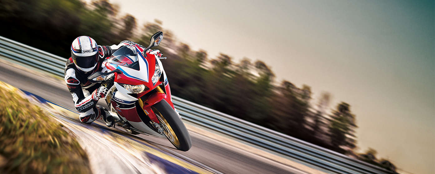 Honda CBR1000RR motorbike front-threequarter view with rider, leaning into bend. Left-facing (Race track location).