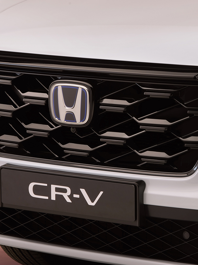 Gros plan sur la calandre avant d'un Honda CR-V, présentant un motif en nid d'abeille noir avec le logo Honda au centre et le nom du modèle CR-V visible en dessous.