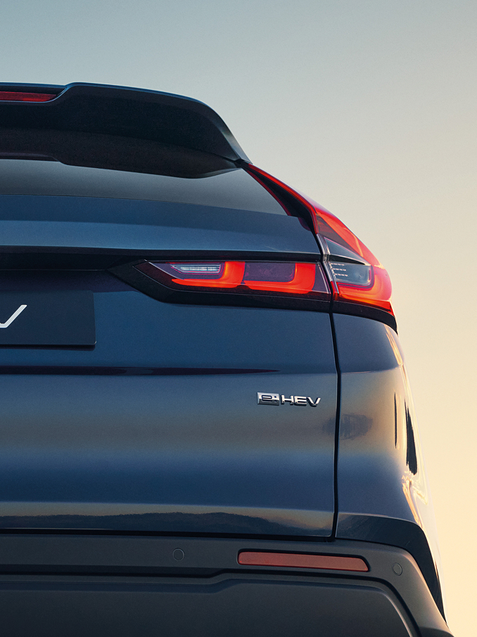 Gros plan arrière d'un Honda CR-V e:HEV bleu foncé montrant le logo Honda, l'inscription CR-V et les feux arrière à LED illuminés sur un doux ciel de coucher de soleil.