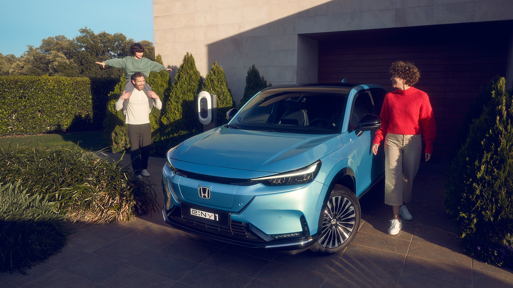 Famille se tenant debout à côté d’un Honda e:Ny1 vu de face à l’avant et stationné à l’extérieur d’une maison.
