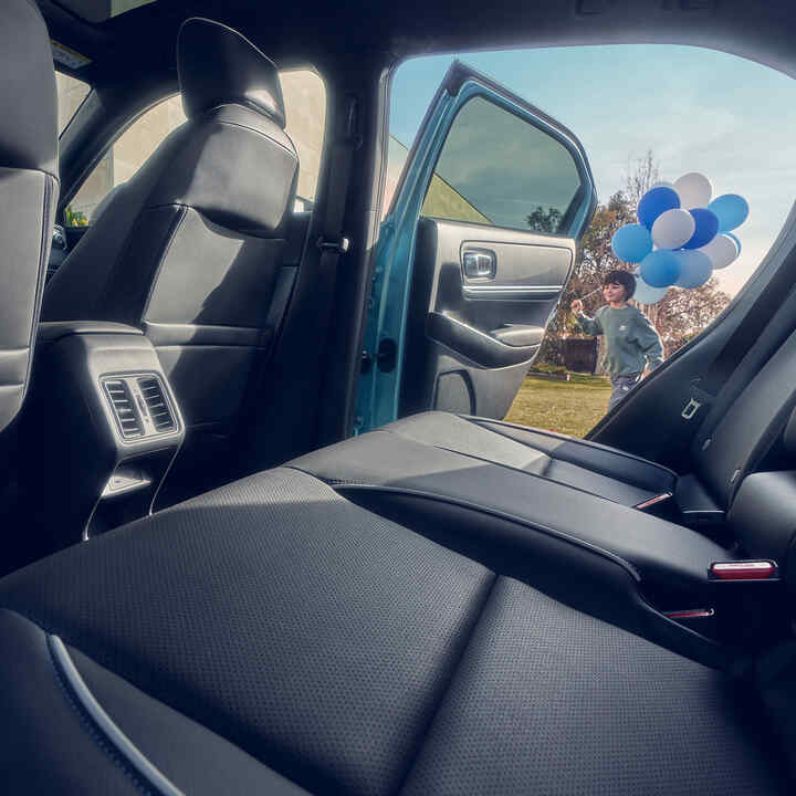 Gros plan sur le siège arrière du Honda e:Ny1 avec enfant passant devant une porte ouverte en portant des ballons.