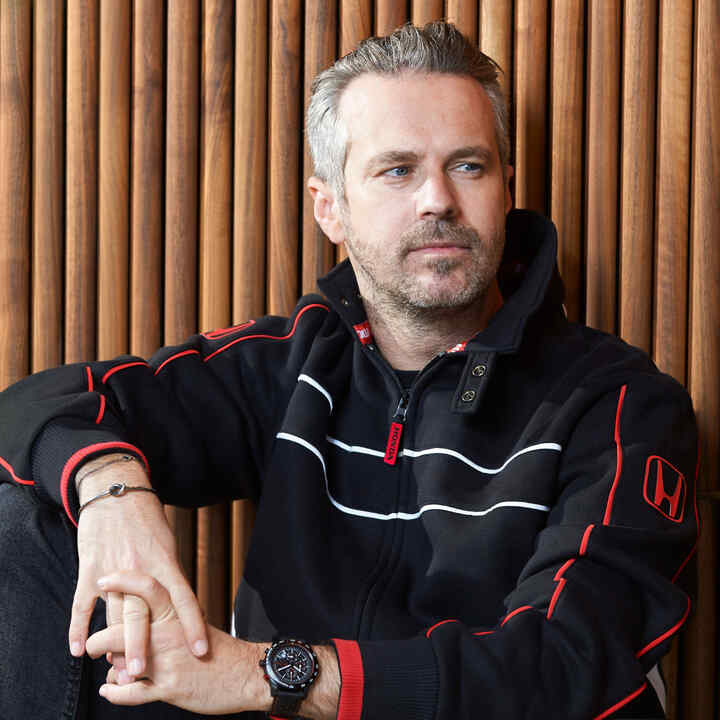 Un homme portant une casquette et une veste Honda Racing, et qui touche le bord de sa casquette.