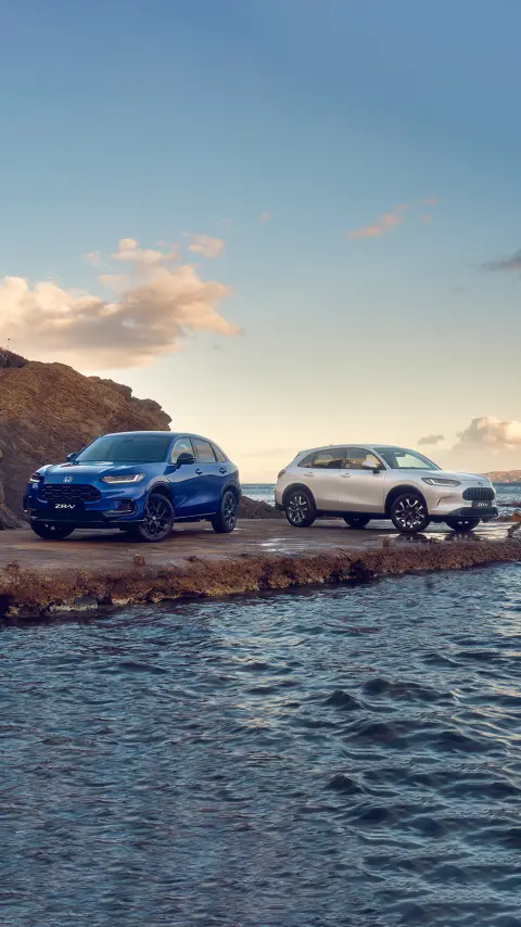 Vue de trois quarts avant de deux voitures hybrides ZR-V stationnées en montagne.