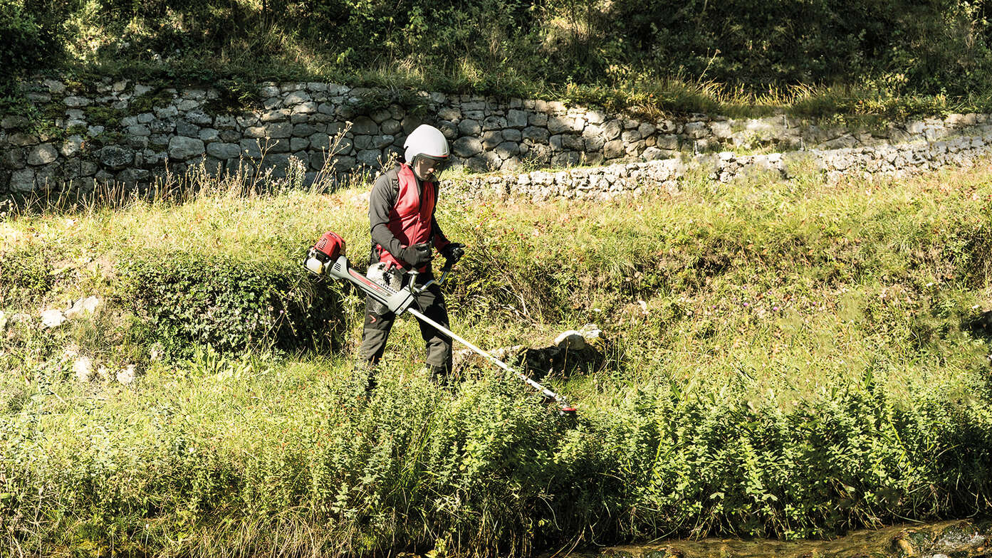 Débroussailleuse utilisée par un homme à côté d'un ruisseau