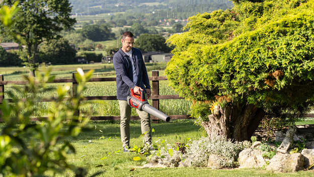 Homme tenant et utilisant un souffleur sans fil dans un jardin
