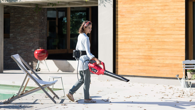 Model wearing Honda cordless belt and using a leaf blower in a garden location.