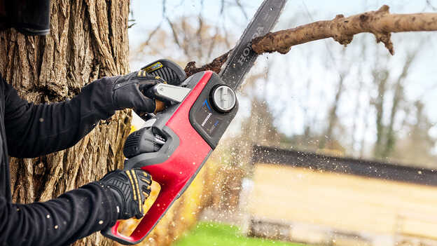 Gros plan d'un modèle coupant une branche d'arbre avec une tronçonneuse sans fil.