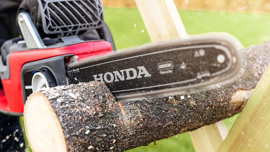 Gros plan d'un modèle coupant du bois avec une tronçonneuse sans fil Honda.