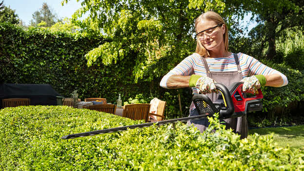 Femme taillant une haie avec un taille-haie sans fil Honda dans un jardin.