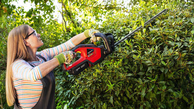 Femme taillant des buissons avec un taille-haie sans fil Honda dans un jardin.