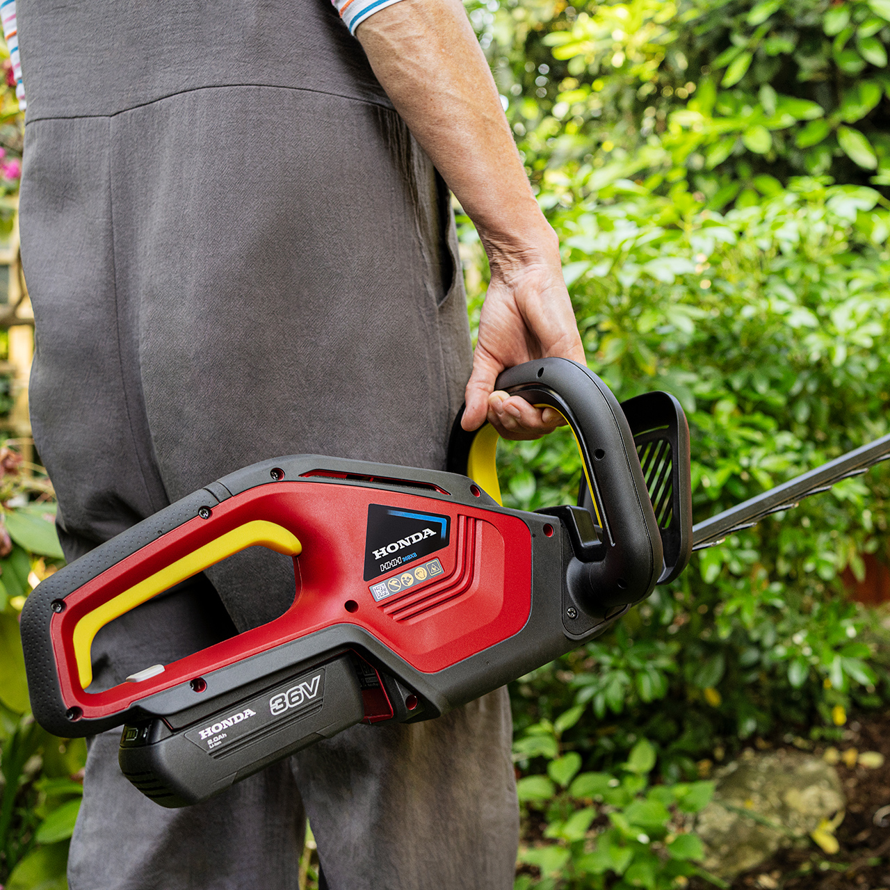 Modèle tenant un taille-haie sans fil Honda dans un jardin.