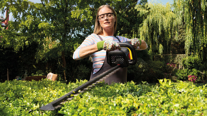 Femme utilisant un taille-haie sans fil Honda pour tailler une haie dans un jardin.