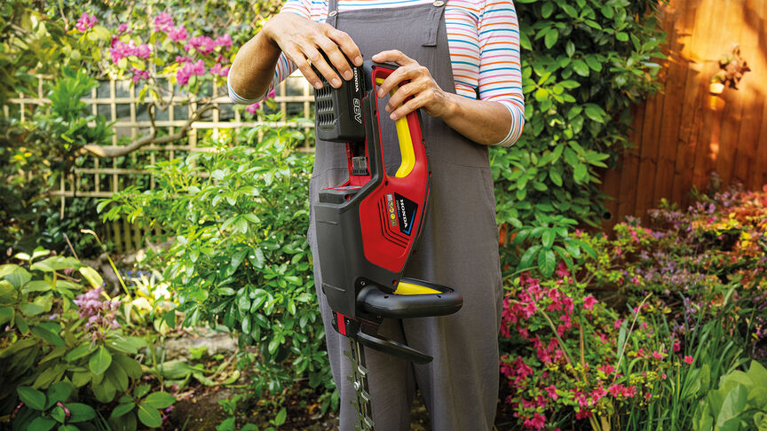 Femme utilisant un taille-haie sans fil Honda pour tailler une haie dans un jardin.