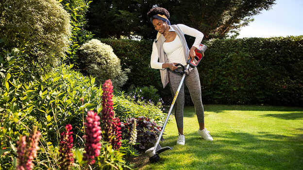 Femme utilisant le coupe-bordure sans fil Honda sur la pelouse d’un jardin pour montrer que les plantes sont protégées.