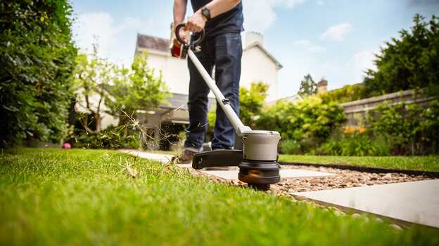 Homme utilisant le coupe-bordure sans fil Honda sur la pelouse d‘un jardin.