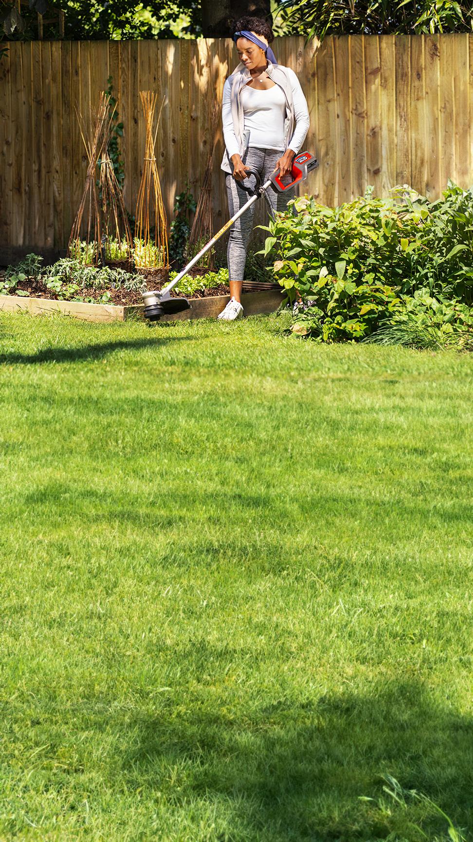 Modèle tenant un coupe-bordure sans fil Honda dans un jardin.
