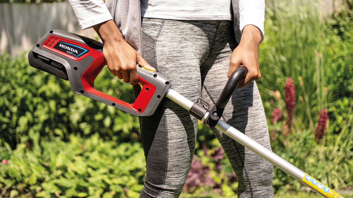 Gros plan sur une femme utilisant un coupe-bordure sans fil Honda dans un jardin.