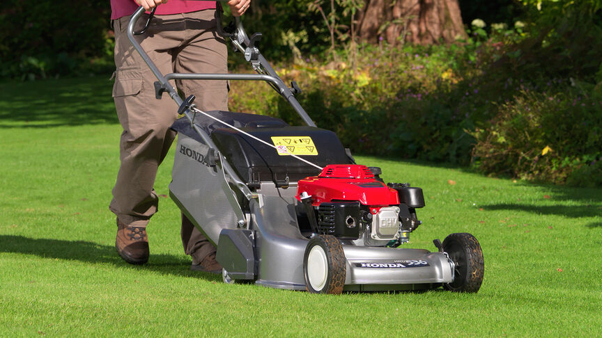 Un homme dans un jardin tondant la pelouse avec une tondeuse à gazon Honda HRD.