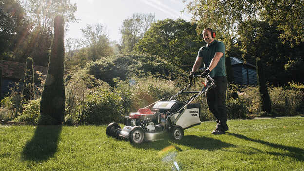 Homme tondant avec une tondeuse à gazon HRH dans un jardin.