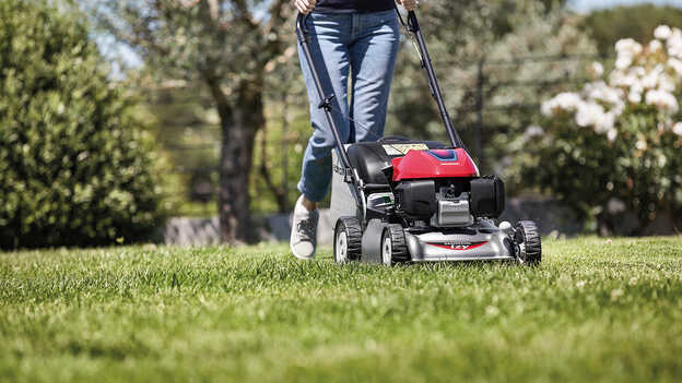 Vue latérale de la tondeuse à gazon Honda IZY avec femme dans jardin