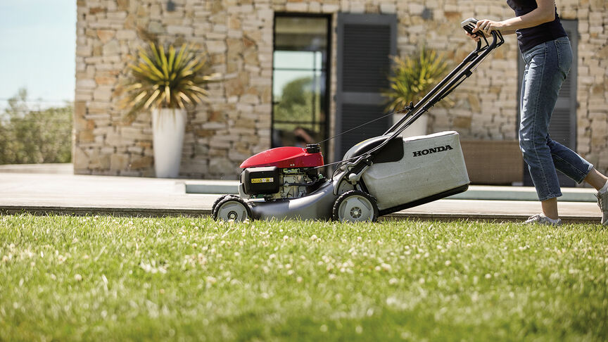 Vue latérale de la tondeuse à gazon Honda IZY avec femme dans jardin