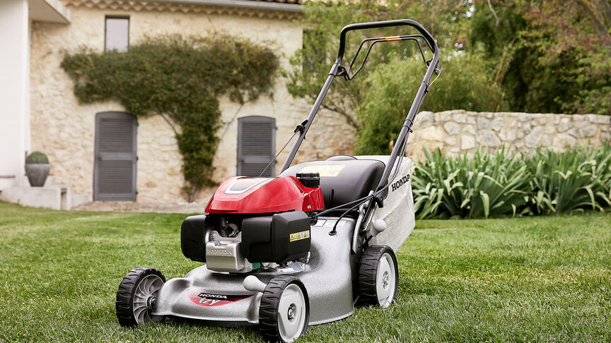 Vue latérale de la tondeuse à gazon Honda IZY avec femme dans jardin