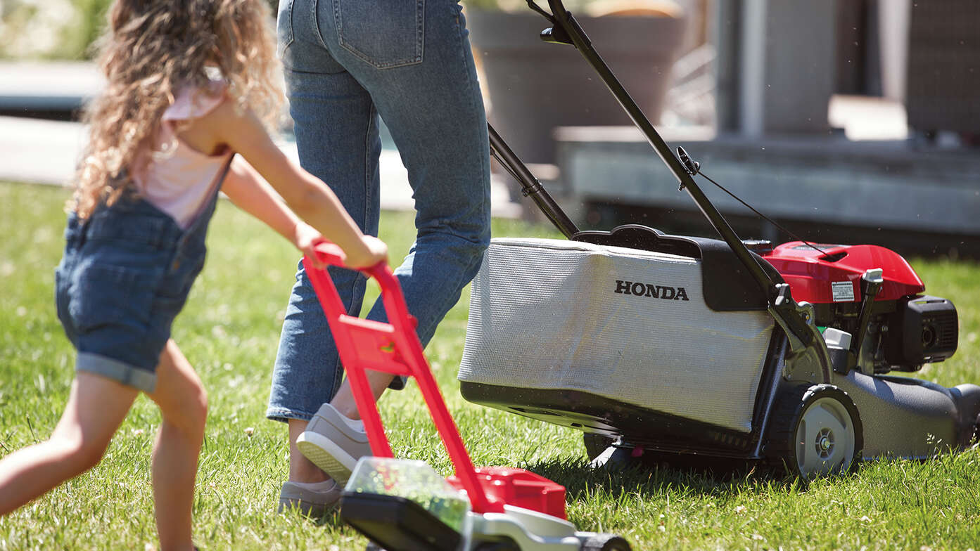 Vue latérale de la tondeuse à gazon Honda IZY avec femme et enfant dans jardin