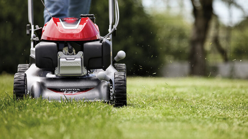 Vue latérale de la tondeuse à gazon Honda IZY avec femme dans jardin