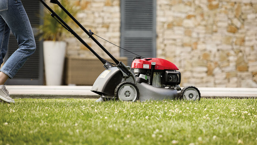 Vue latérale de la tondeuse à gazon Honda IZY avec femme dans jardin