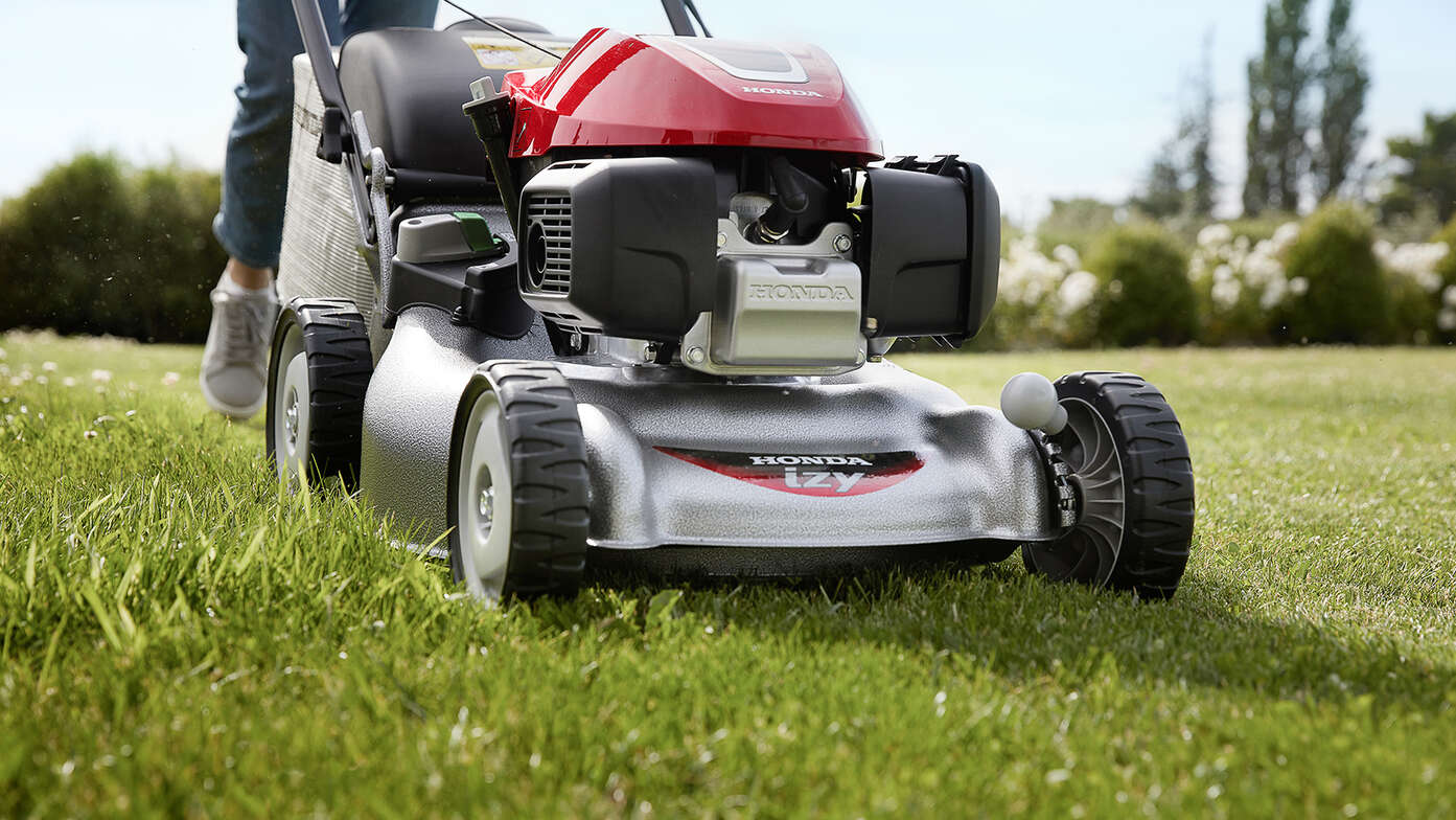 Vue latérale de la tondeuse à gazon Honda IZY avec femme dans jardin