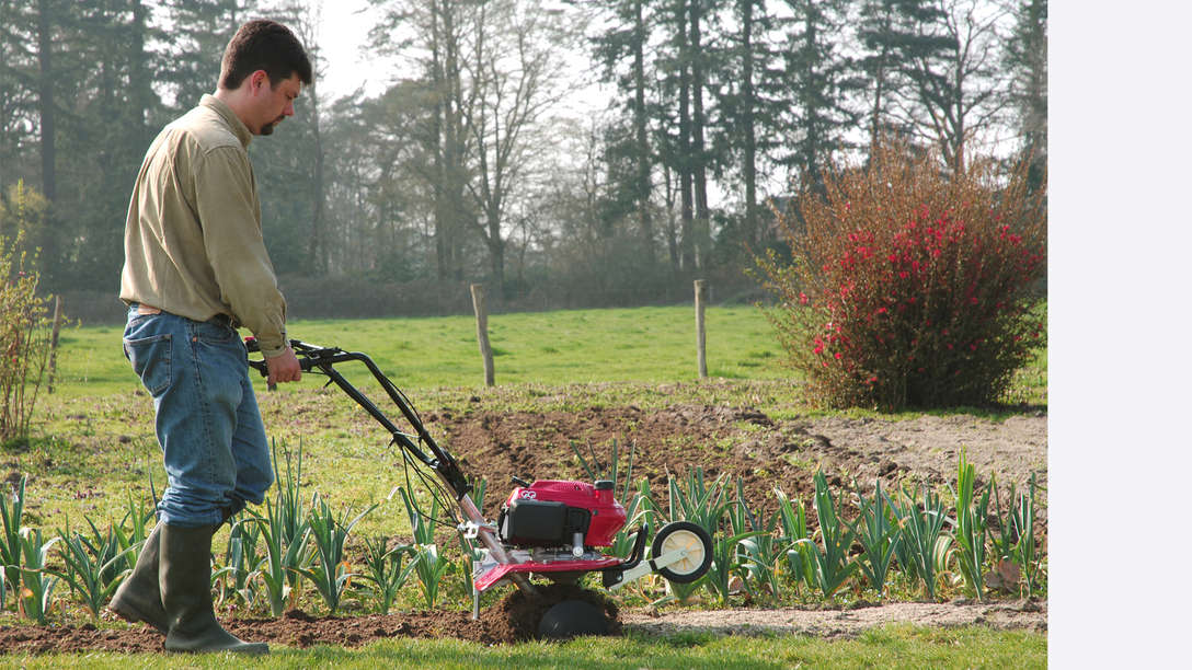 Motobineuse, tournée vers la droite, utilisée par un démonstrateur, dans un jardin.
