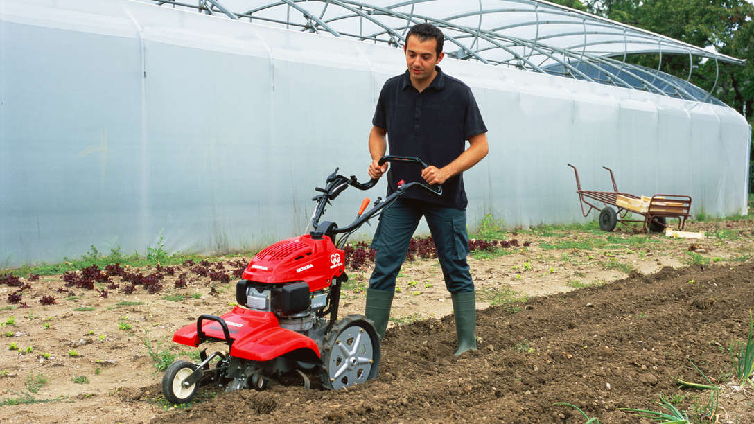 Motobineuse équipée d'outils rotatifs utilisée par un démonstrateur dans un jardin.