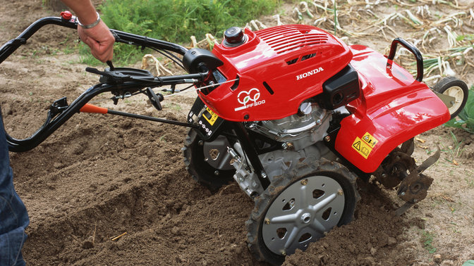 Gros plan de la motobineuse équipée d'outils rotatifs mettant en évidence le guidon réglable, dans un jardin.