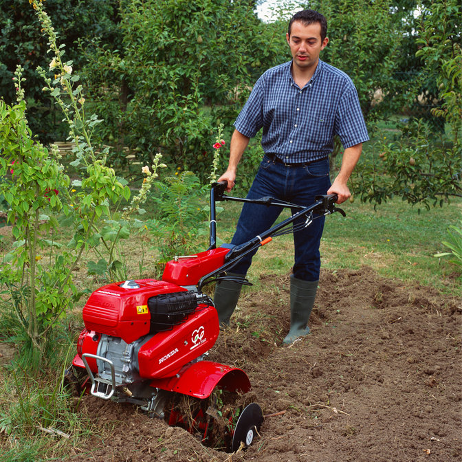 Motoculteur transformable utilisé par un démonstrateur dans un jardin.