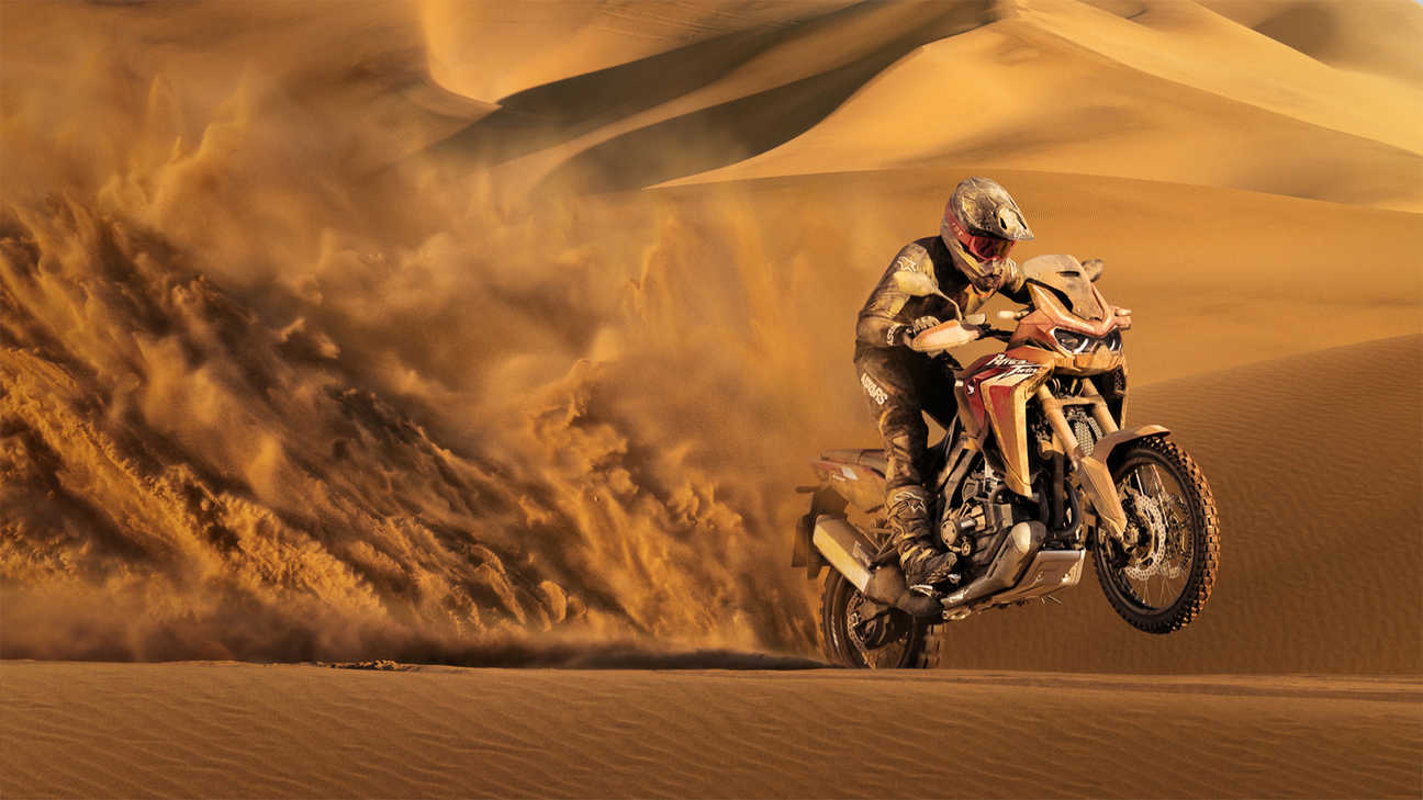 Vue de trois quarts avant droit de la Honda Africa Twin, moto sale pilotée dans le sable