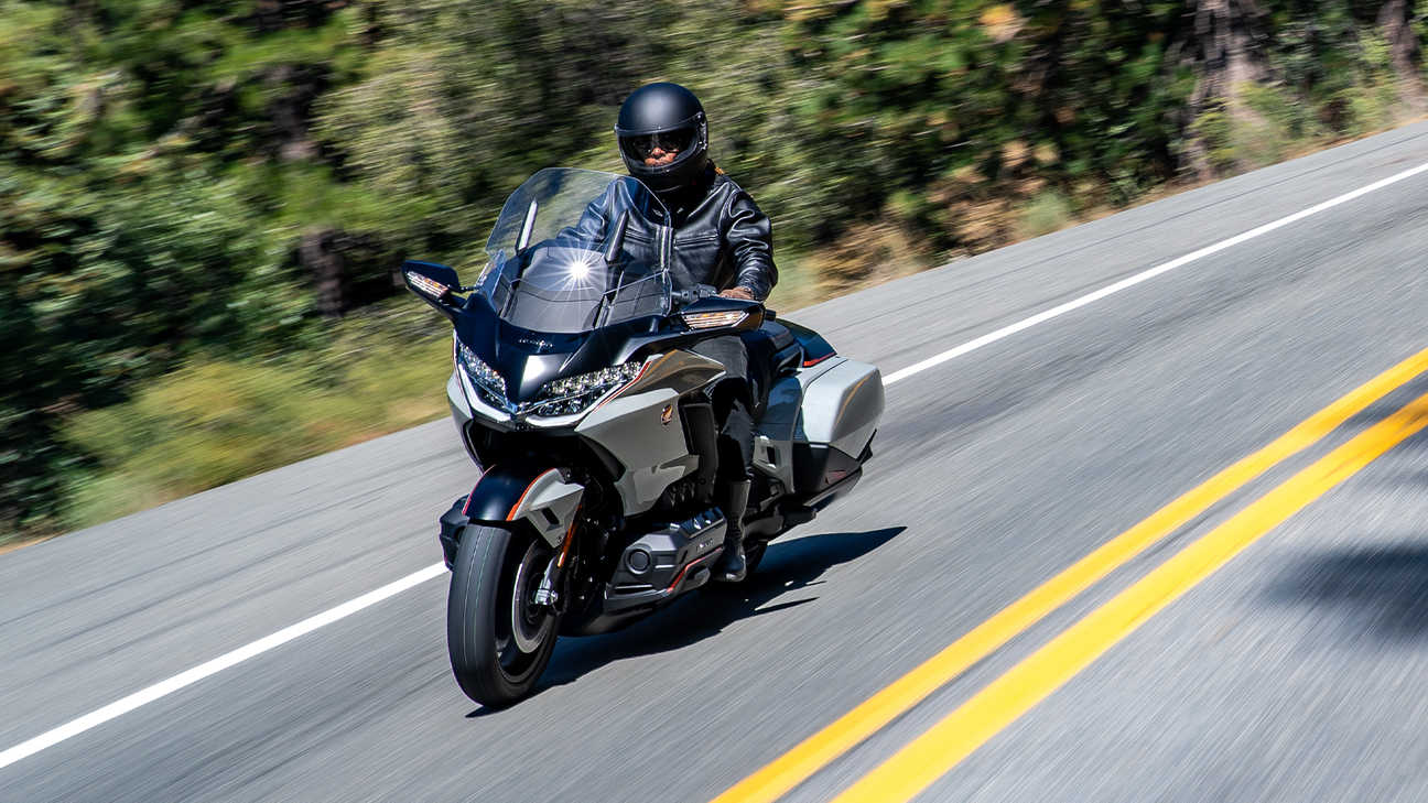 Vue de trois quarts avant gauche de la Honda GL1800 Gold Wing Standard Pearl Deep Mud Grey avec motard sur une route de campagne