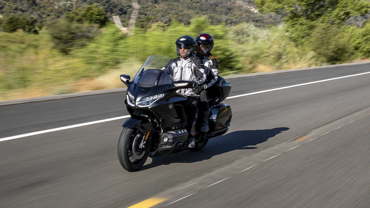 Vue de trois quarts avant gauche de la GL1800 Gold Wing Tour 3 en noir métallisé bronze à canon, avec conducteur et passager sur une route de campagne
