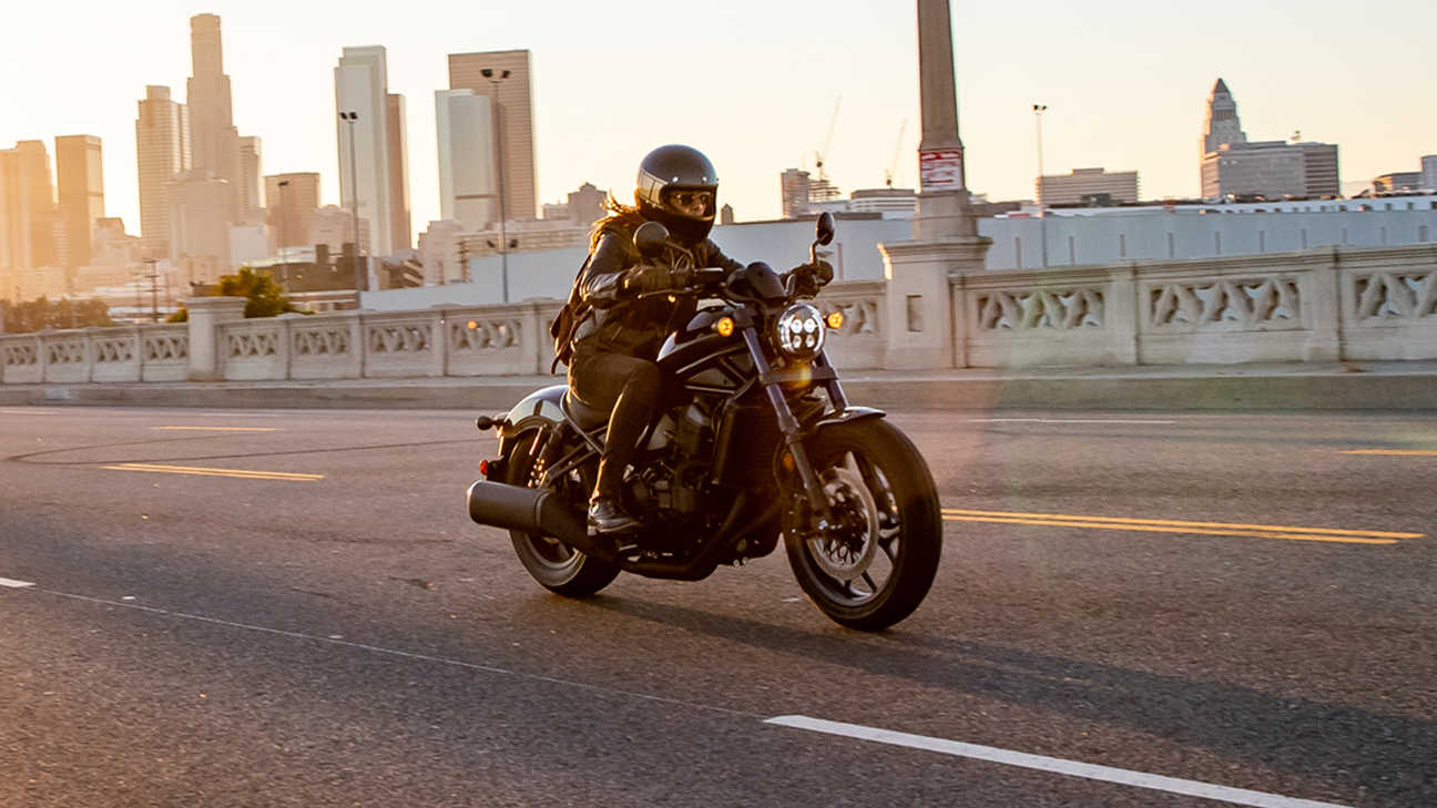 Vue de trois quarts avant droit de la Honda CMX1100 Rebel avec motard en milieu urbain en plein jour