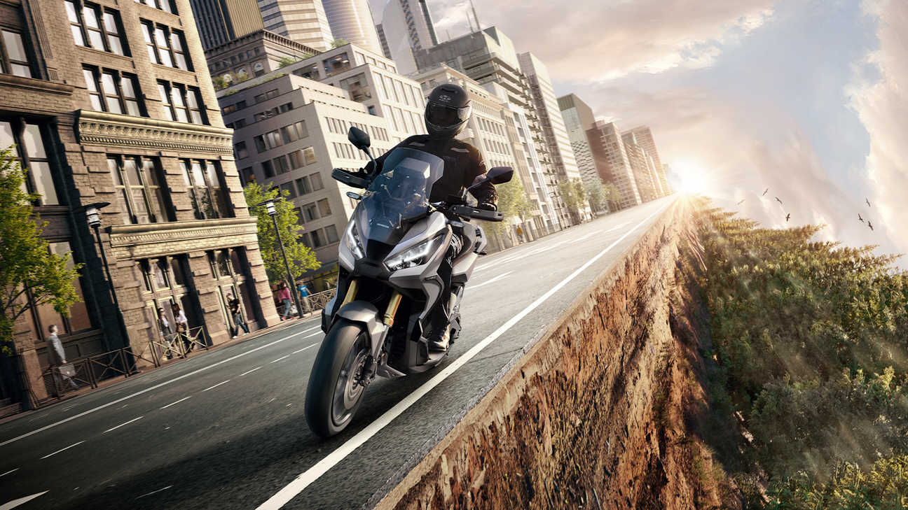 Vue de trois quarts avant gauche de la Honda X-ADV 3 en gris avec motard entre ville et forêt