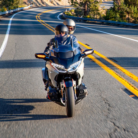 Vue avant de la Honda GL1800 Gold Wing Pearl Deep Mud Grey avec conducteur et passager sur une route de campagne