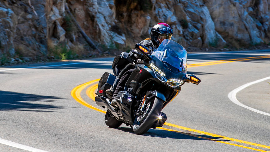 Vue de trois quarts avant droit de la Honda GL1800 Gold Wing Tour en noir métallisé avec motard et passager sur une route de montagne