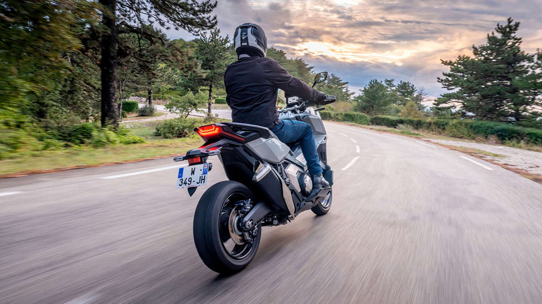 Vue de trois quarts arri&egrave;re droit de la Honda X-ADV en gris, avec motard sur une route de campagne