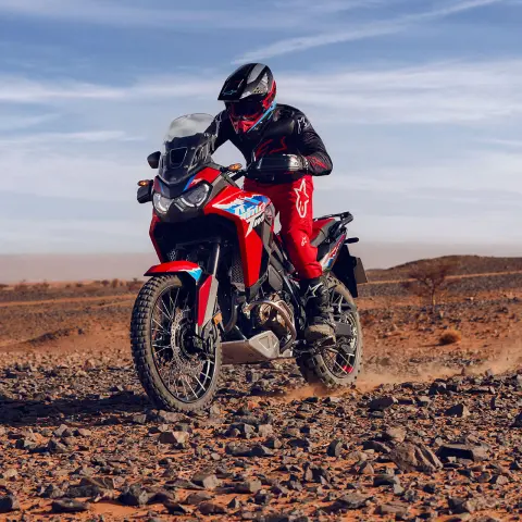 Modèle conduisant une moto CRF1100L Africa Twin sur un terrain rocheux dans un environnement désertique.
