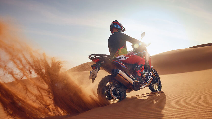 Mannequin roulant à bord d’une moto CRF1100L Africa Twin dans un environnement désertique.