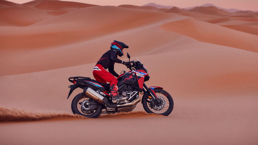 Mannequin roulant à bord d’une moto CRF1100L Africa Twin dans un environnement désertique.