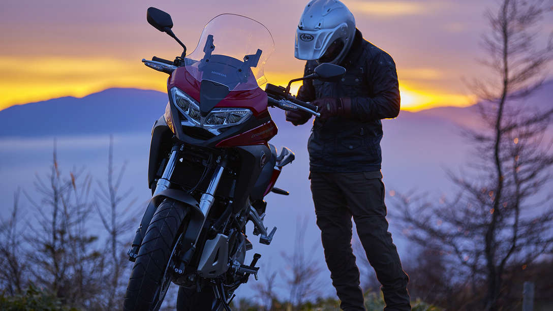 VFR800X à l'arrêt dans un paysage de campagne avec un pilote à côté.